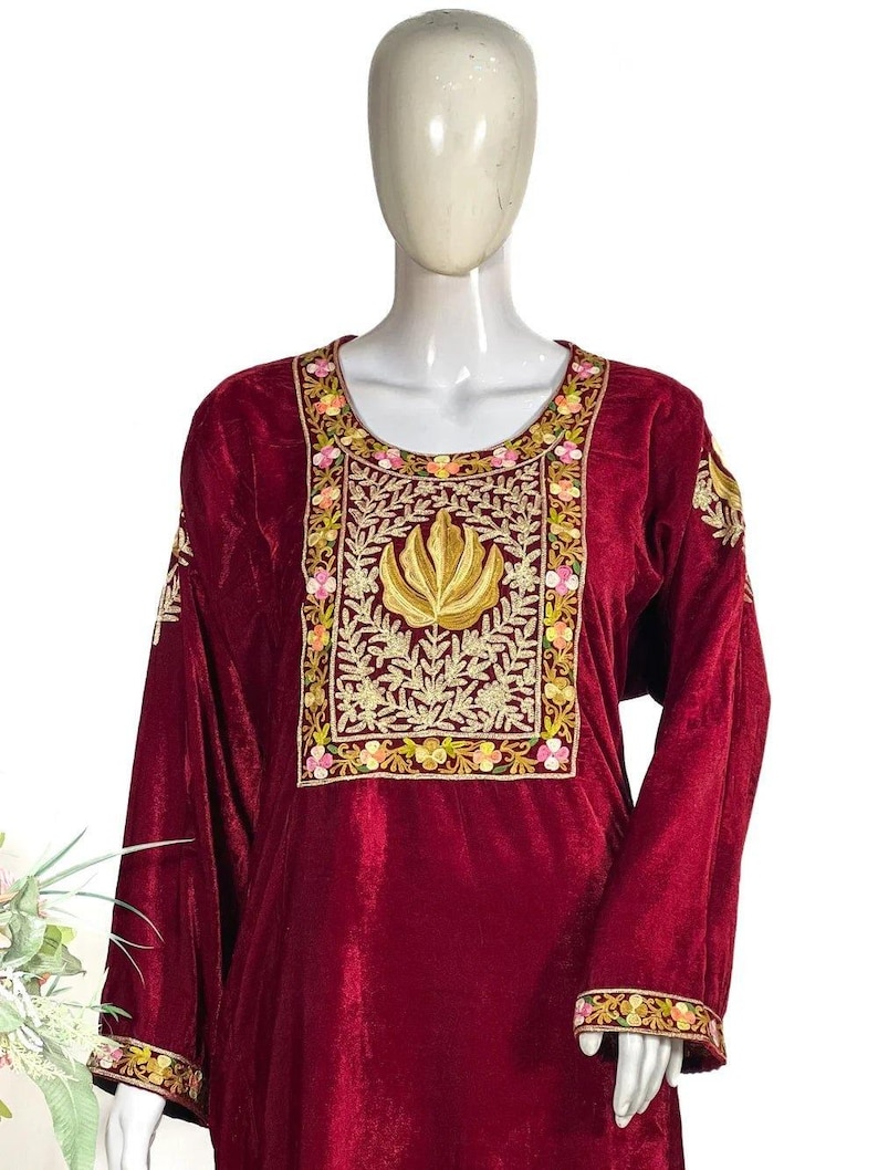 May include: A deep maroon velvet tunic featuring a prominent rectangular chest panel with intricate gold thread embroidery depicting a central lotus motif surrounded by floral patterns in pink, yellow, and green. The long sleeves have matching trim.