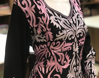 May include: A black long-sleeved tunic featuring a V-neckline and intricate embroidery in shades of light pink and silver. The floral-inspired scrollwork pattern covers the front bodice and extends down the sleeves, creating a detailed contrast.