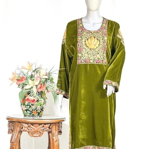 May include: An olive green velvet tunic featuring a scoop neckline and long sleeves. The garment is decorated with intricate floral embroidery in pink, yellow, and green thread around the neckline, cuffs, and hem, with a central golden leaf motif.