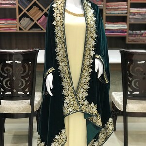 May include: A dark green velvet shawl with intricate white and gold embroidery. The shawl is draped over a mannequin wearing a cream-colored dress.