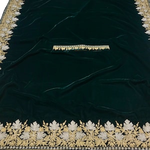 May include: A dark green velvet fabric with a gold and silver embroidered border. The border features a repeating pattern of leaves and flowers.