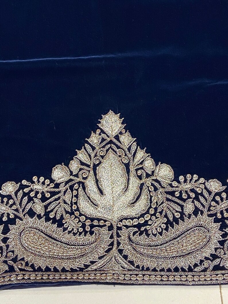 May include: A dark blue velvet fabric with a silver embroidered border. The border features a floral design with paisley shapes.
