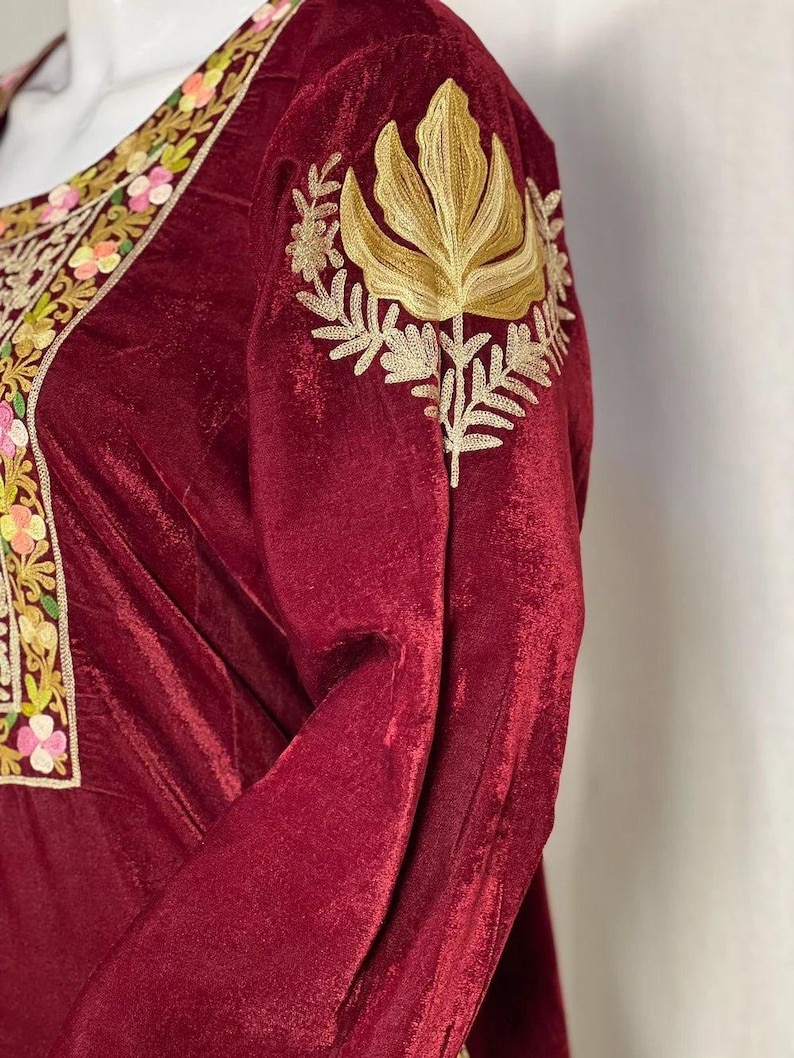 May include: A deep burgundy velvet long-sleeve garment featuring intricate gold thread embroidery on the shoulder and a neckline border decorated with colorful floral patterns in shades of pink, yellow, and green on a cream-colored fabric base.