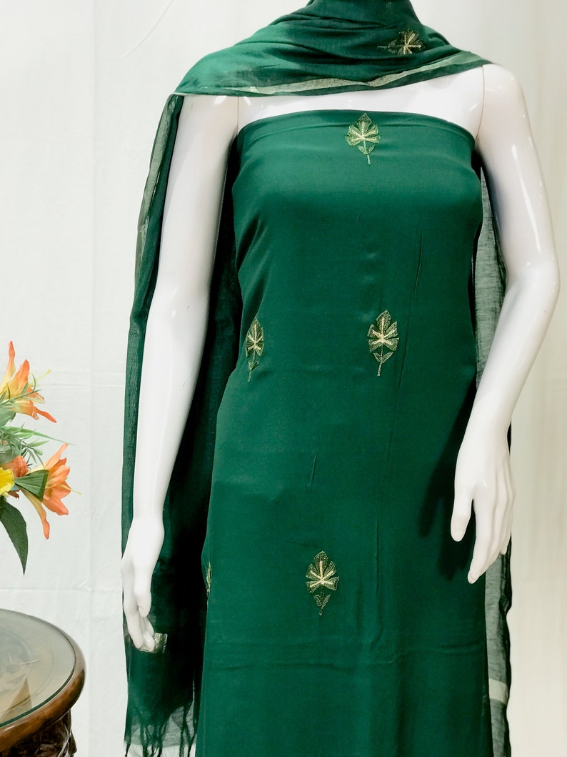 May include: A dark green dress with a leaf pattern embroidered on it. The dress is made of a soft, flowing fabric and has a simple, elegant design.