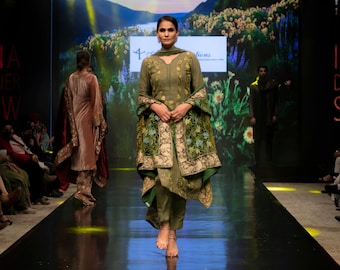 May include: An olive green salwar kameez featuring a long-sleeved tunic with subtle embroidery, matching straight-leg trousers, and a draped shawl adorned with intricate floral patterns in shades of green, gold, and blue, worn with simple sandals.
