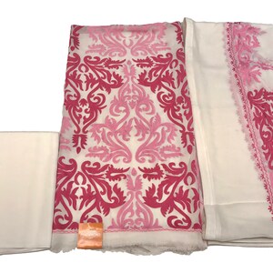 May include: A three-piece fabric set featuring a white base with vibrant pink and light pink damask-style embroidery. The set includes a plain white fabric piece, a large central piece with dense floral patterns, and a sheer white dupatta with pink borders.