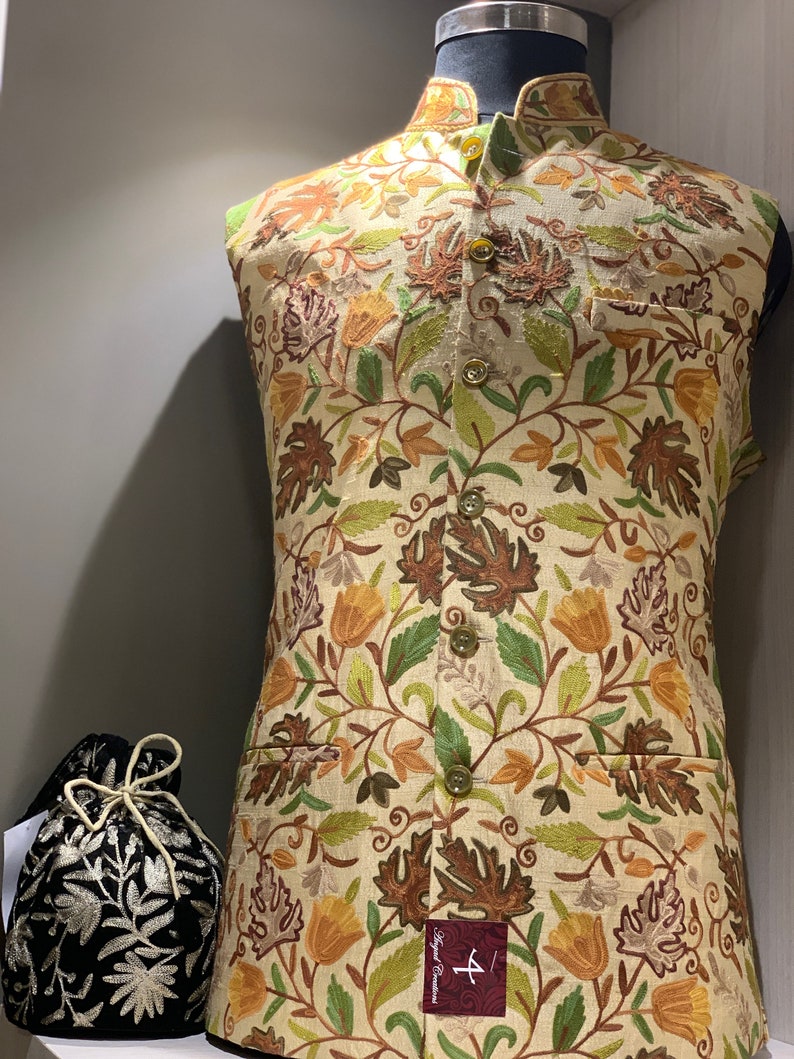 Peut inclure: Un gilet beige sans manches avec un motif floral brod&eacute; dans des tons de brun, vert et jaune. Le gilet a un col mandarin et une fermeture &agrave; boutons. Le gilet est pr&eacute;sent&eacute; sur un mannequin.