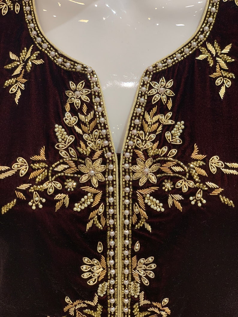 May include: A dark brown velvet fabric with gold and white embroidery. The embroidery features a floral design with leaves and flowers.