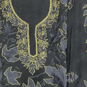May include: A black fabric garment featuring a U-shaped neckline and intricate embroidery. The design consists of golden-yellow thread outlining large, stylized leaf patterns and swirling vine motifs that cover the front of the piece.