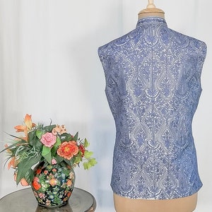 Puede incluir: Un chaleco sin mangas de color azul claro con un estampado floral blanco. El chaleco tiene un cuello mandar&iacute;n y un cierre de bot&oacute;n.
