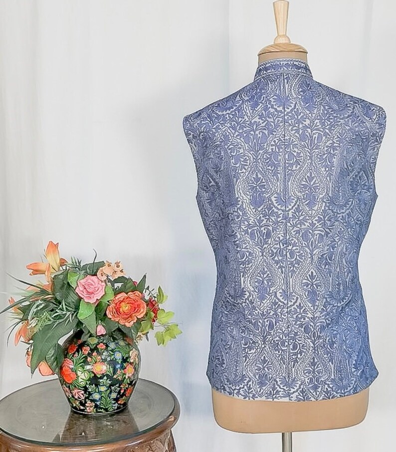 Puede incluir: Un chaleco sin mangas de color azul claro con un estampado floral blanco. El chaleco tiene un cuello mandar&iacute;n y un cierre de bot&oacute;n.