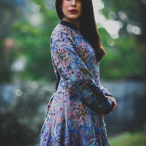 May include: A woman wearing a long-sleeved dress with a floral pattern in shades of blue, pink, and green. The dress has a fitted bodice and a flowing skirt.