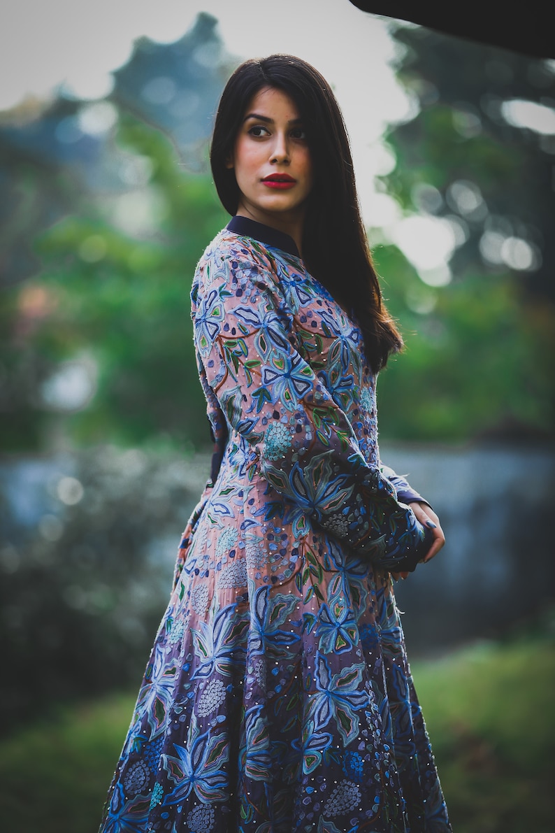 May include: A woman wearing a long-sleeved dress with a floral pattern in shades of blue, pink, and green. The dress has a fitted bodice and a flowing skirt.