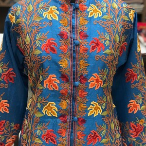 May include: A long-sleeved, blue embroidered jacket with a mandarin collar and button closure. The embroidery features a floral design in shades of orange, red, and green.