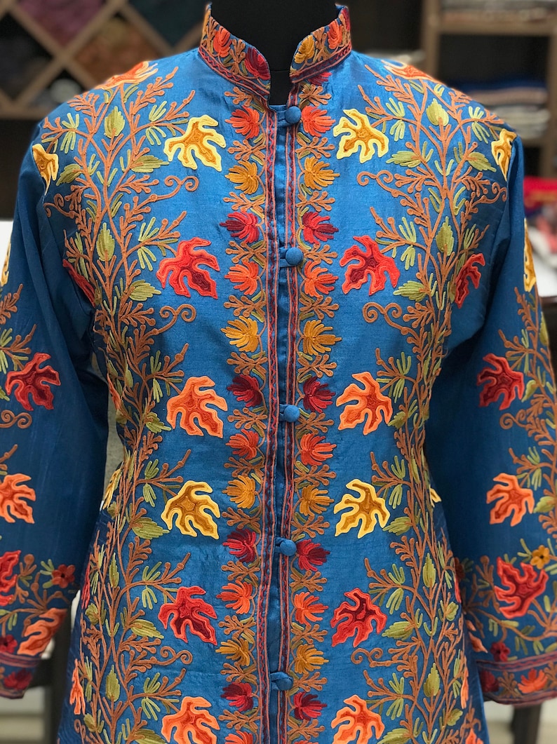 May include: A long-sleeved, blue embroidered jacket with a mandarin collar and button closure. The embroidery features a floral design in shades of orange, red, and green.