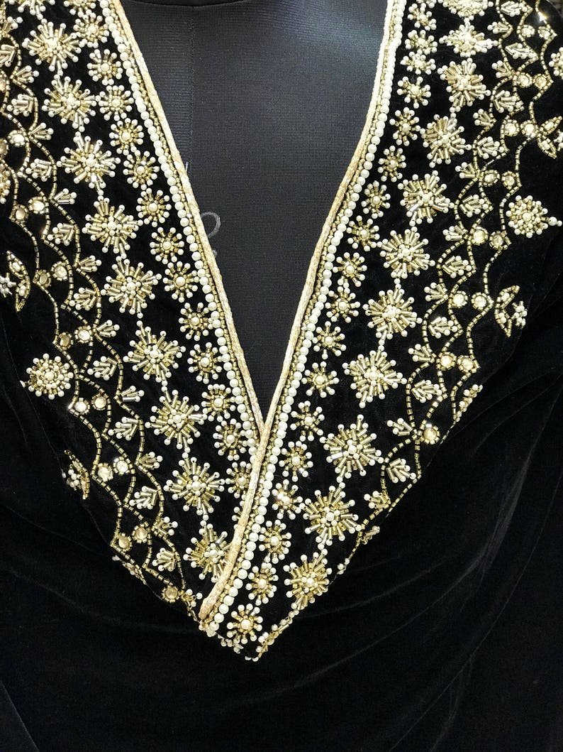 Puede incluir: Primer plano de una tela de terciopelo negro con un escote de cuentas doradas y blancas. El escote presenta un patr&oacute;n repetitivo de peque&ntilde;as estrellas y perlas.