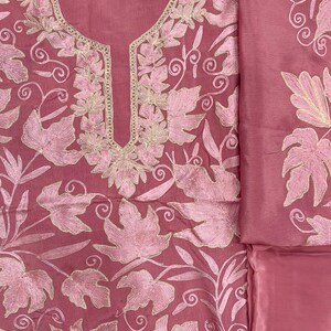 May include: A dusty rose garment featuring intricate light pink leaf embroidery across the fabric. The neckline is accented with a gold-toned metallic thread border. The design includes a matching piece of fabric with similar leaf embroidery.