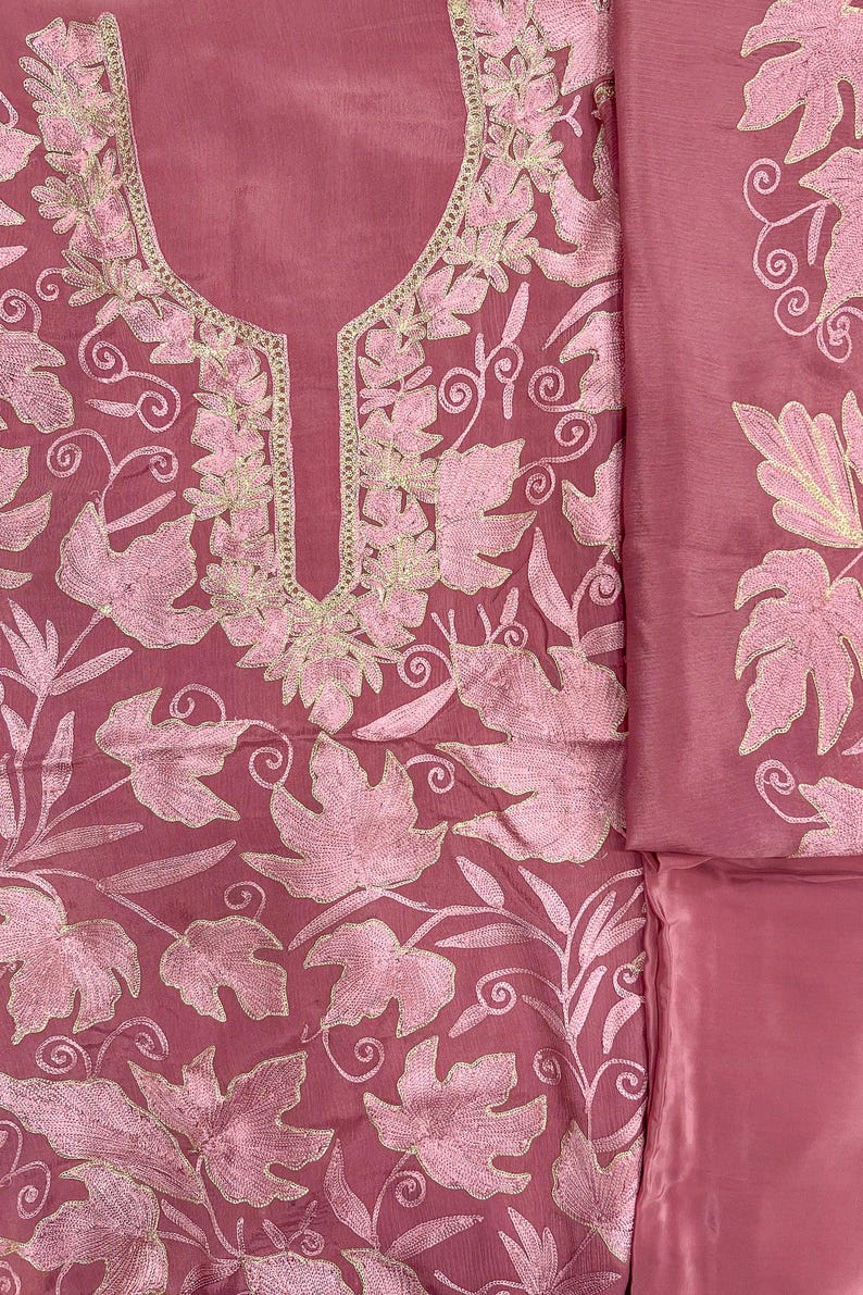 May include: A dusty rose garment featuring intricate light pink leaf embroidery across the fabric. The neckline is accented with a gold-toned metallic thread border. The design includes a matching piece of fabric with similar leaf embroidery.