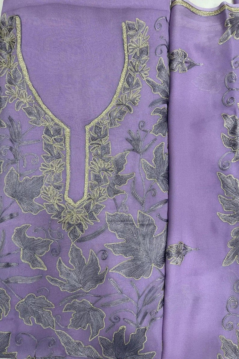 May include: A light purple fabric garment featuring intricate dark purple leaf embroidery and a gold-toned metallic trim around the neckline. The material has a sheer, lightweight texture with a repeating botanical pattern across the surface.