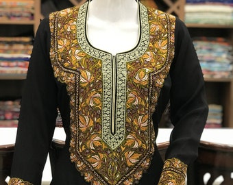 May include: A black long-sleeved tunic featuring an intricate, multi-colored floral embroidery pattern around the neckline, down the center front, and on the cuffs. The embroidery includes shades of olive green, gold, and cream with dark outlines.