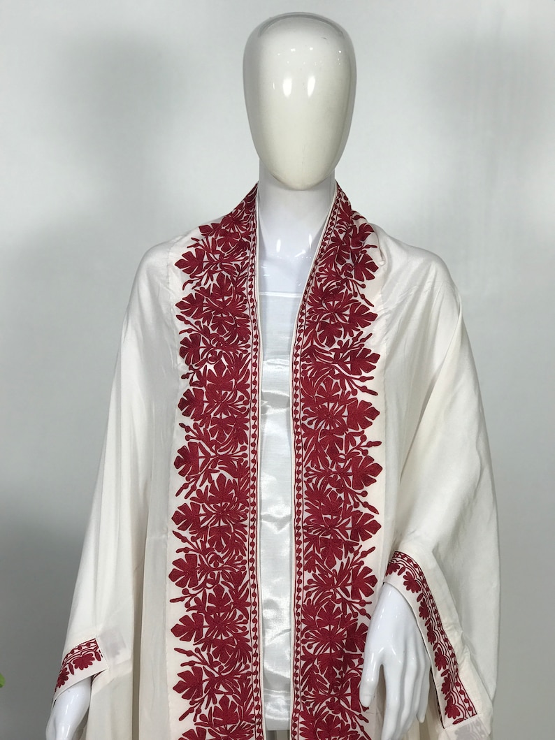May include: White shawl with red embroidered floral designs along the edges.