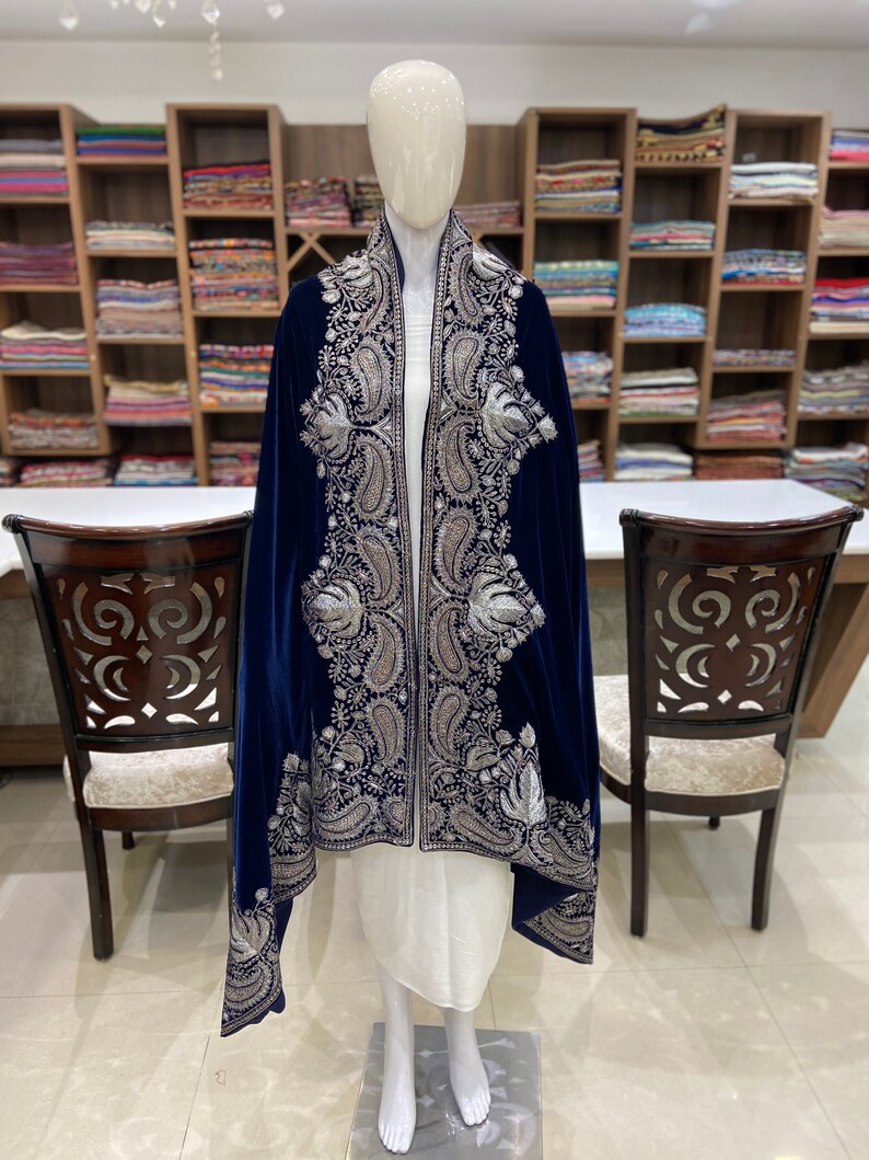 May include: A navy blue velvet shawl with silver embroidery. The shawl has a paisley pattern and is draped over a white dress form.