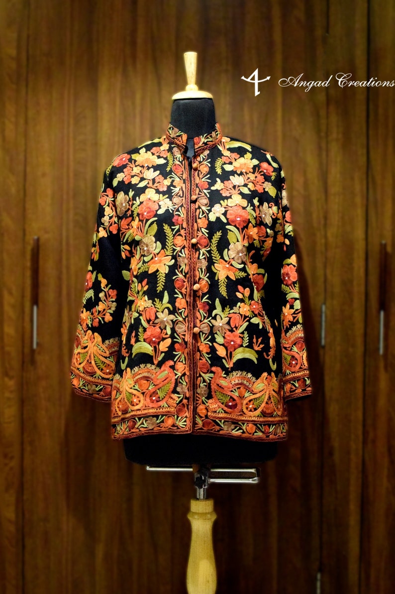 May include: Black jacket with detailed floral embroidery in orange, red, and green. It has a mandarin collar and a button-down front. The sleeves and hem are also decorated with patterns. The text "4 Angad Creations" is visible.