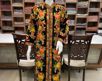 May include: A black long-sleeved coat featuring a vibrant floral embroidery pattern in shades of orange, yellow, and green. The garment has a high collar, a central vertical button placket with matching buttons, and a straight hemline.