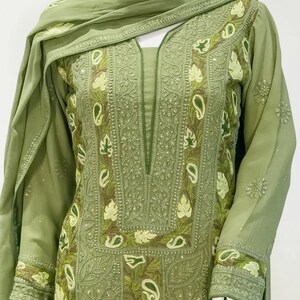 May include: A sage green long-sleeved tunic featuring an intricate embroidered neckline and sleeve cuffs with light green leaf and paisley motifs. The garment includes a matching draped scarf, showcasing detailed needlework and tonal stitching.