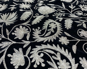 Puede incluir: Tela de terciopelo negro con un patrón de bordado floral plateado. La tela es suave y lujosa, y el bordado es intrincado y detallado.