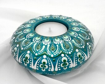 May include: Teal blue candle holder with a white mandala design. The holder has a round shape and a small opening in the centre for a tea light candle.