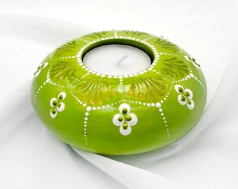 May include: A green ceramic candle holder with white and gold floral designs. The holder has a round shape and a small opening in the centre for a tea light candle.