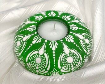 May include: A green candle holder with a white mandala design. The holder has a round shape and a small opening in the centre for a tea light candle.