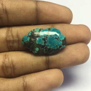 Puede incluir: Una piedra preciosa turquesa en cabujón con una matriz marrón oscura. La piedra tiene una superficie lisa y pulida y una forma irregular única.