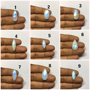 Op de afbeelding: Negen regenboogkleurige maansteen-cabochons in verschillende druppel- en marquisevormen. De stenen worden op een hand getoond, waarbij elke steen van 1 tot 9 is genummerd.