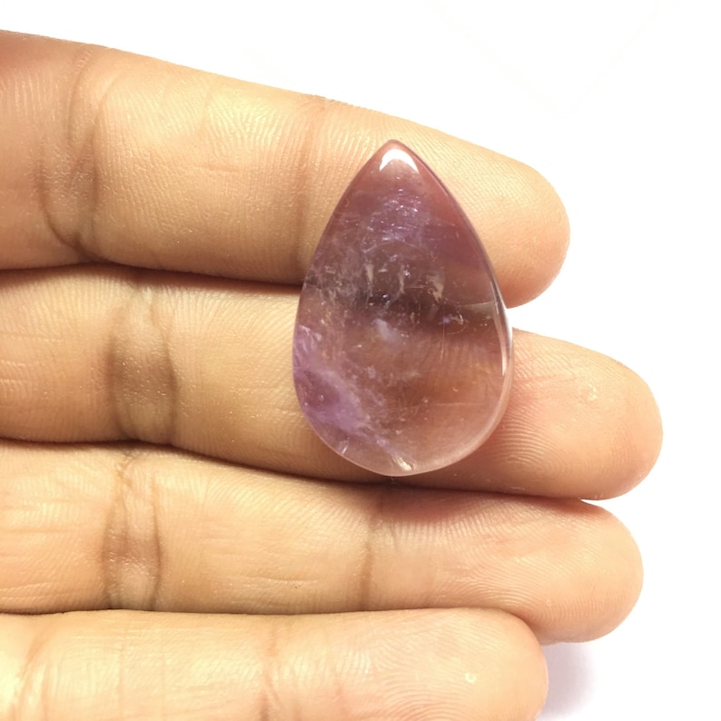 Puede incluir: Un cabuj&oacute;n de piedra preciosa amatista en forma de l&aacute;grima con un color morado y rosa.