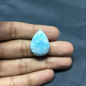 May include: A teardrop-shaped cabochon of blue and white larimar, a gemstone known for its unique marbled pattern.