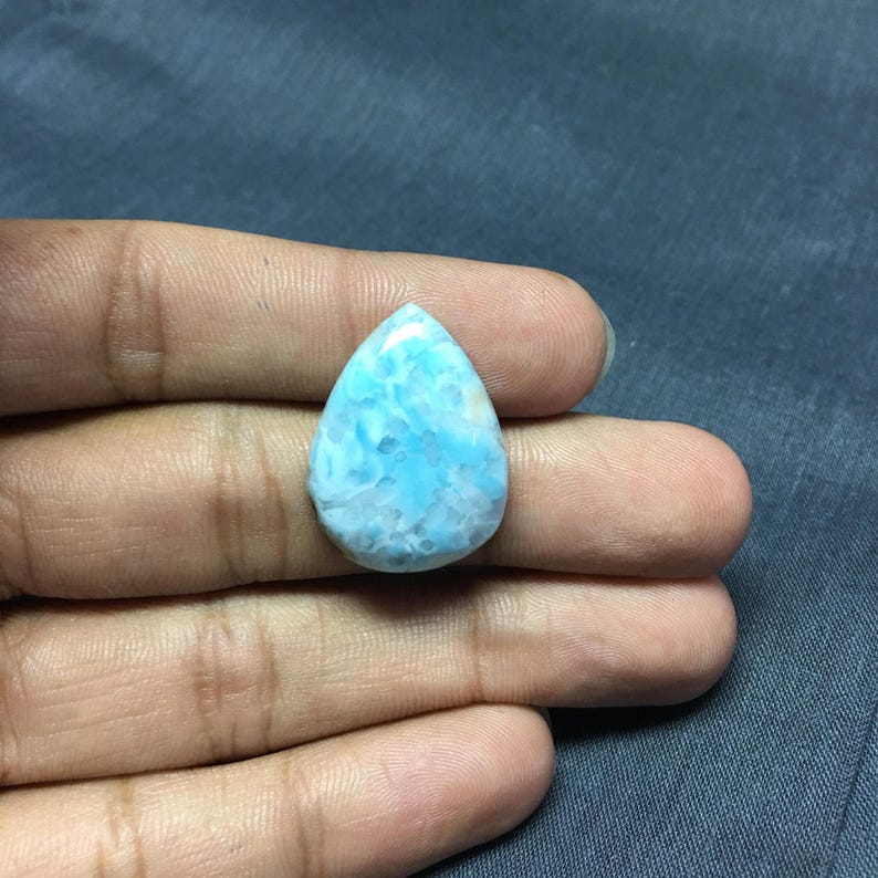 May include: A teardrop-shaped cabochon of blue and white larimar, a gemstone known for its unique marbled pattern.