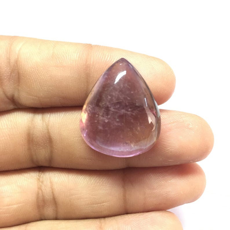 Puede incluir: Una piedra preciosa cabuj&oacute;n en forma de l&aacute;grima con un degradado de color p&uacute;rpura y rosa. La piedra preciosa es lisa y pulida.