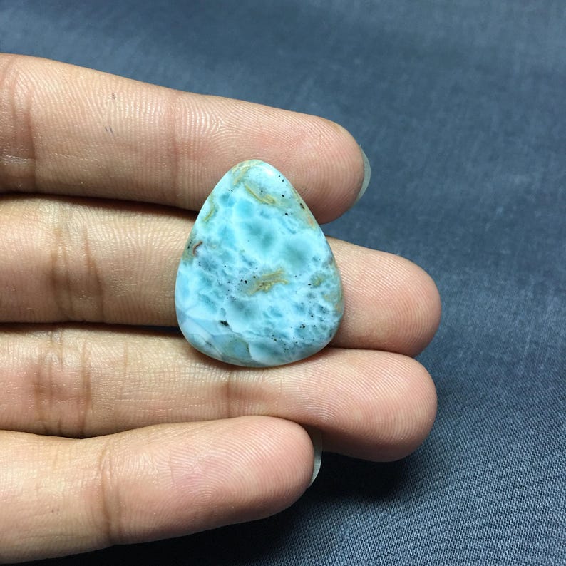 May include: A teardrop-shaped cabochon of blue and white ocean jasper with brown inclusions. The stone is smooth and polished.