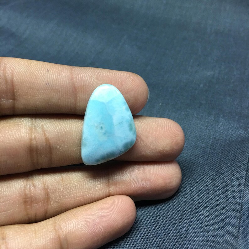 May include: A light blue, triangular shaped, cabochon gemstone with a cloudy, marbled pattern.