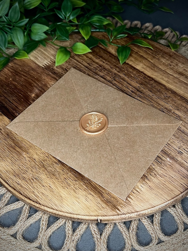 Puede incluir: Un sobre de papel marr&oacute;n con un sello de lacre dorado con un dise&ntilde;o floral.