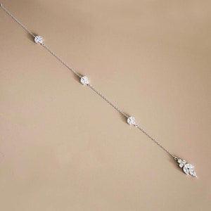 May include: A delicate silver chain necklace with three small, round, crystal-encrusted charms and a larger, dangling crystal charm at the end.