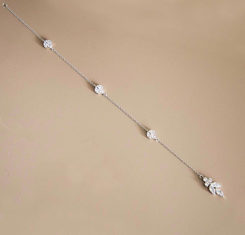 May include: A delicate silver chain necklace with three small, round, crystal-encrusted charms and a larger, dangling crystal charm at the end.