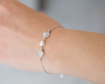 May include: A delicate silver bracelet with a pearl and crystal accents. The bracelet features a simple chain design with three small leaf-shaped charms.