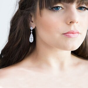May include: A pair of silver teardrop earrings with a clear crystal design. The earrings are dangling and have a small round crystal at the top.