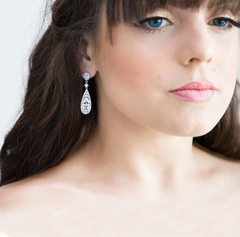 May include: A pair of silver teardrop earrings with a clear crystal design. The earrings are dangling and have a small round crystal at the top.