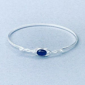 May include: A silver bangle bracelet with a dark blue oval-shaped stone set in a Celtic knot design.