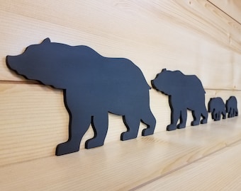 May include: A set of five black bear silhouettes, arranged in a line, with the largest bear at the front and the smallest bear at the back. The bears are made of wood and are painted black.