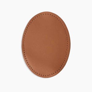 Peut inclure: Un patch ovale en cuir marron avec une couture décorative autour du bord.